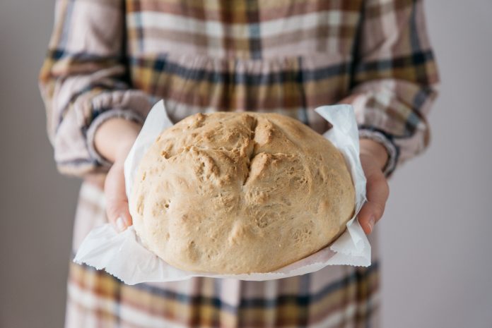 Woman holding tasty fresh handmade bread, in her home, close up