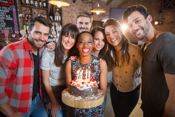 Portrait of happy friends holding birthday cake in restaurant