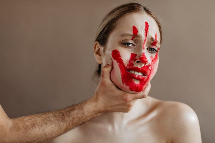 Portrait of crying woman with bloody handprint. Girl is roughly held by throat