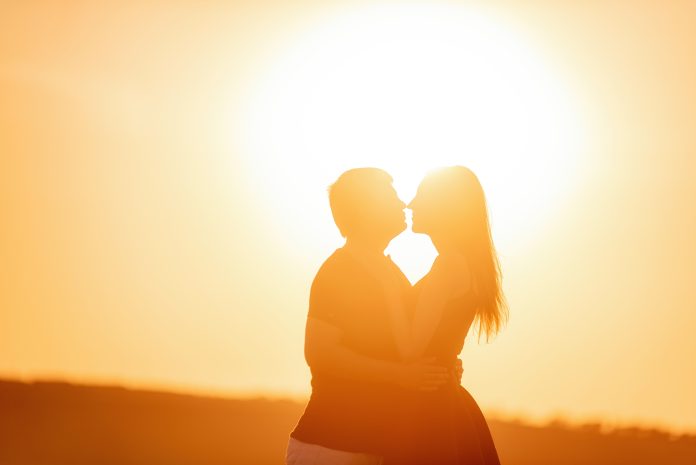 Close-up portrait of a silhouette of a loving couple in the rays of orange sunset. Lovers hug, kiss