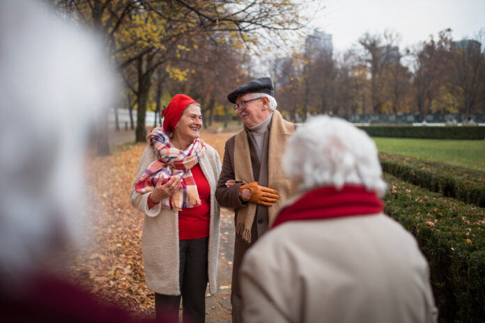 Group of happy senior friends on walk outdoors in town park in autumn, talking and laughing.
