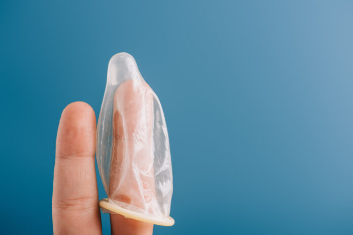 cropped view of fingers with condom isolated on blue, contraception concept