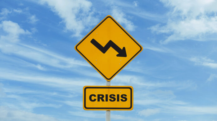 Yellow road sign crisis with arrow down on blue sky with clouds,