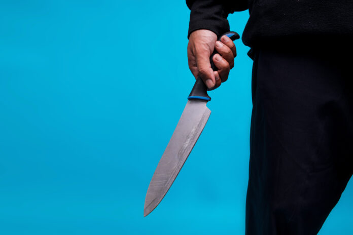 Close-up Of Murderer Holding A Knife On Blue Studio Wall