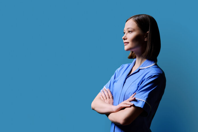 Portrait of young serious female nurse looking in profile on blue background